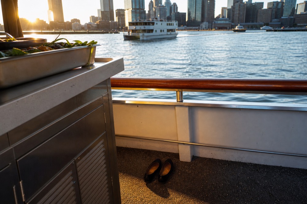 A pair of flat closed-toed shoes beside a buffet counter on a boat deck, warm light and a polished handrail behind.