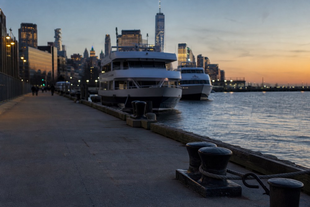 A long empty pier walkway stretching toward moored tour boats at golden hour, bollards and cleats in the foreground.
