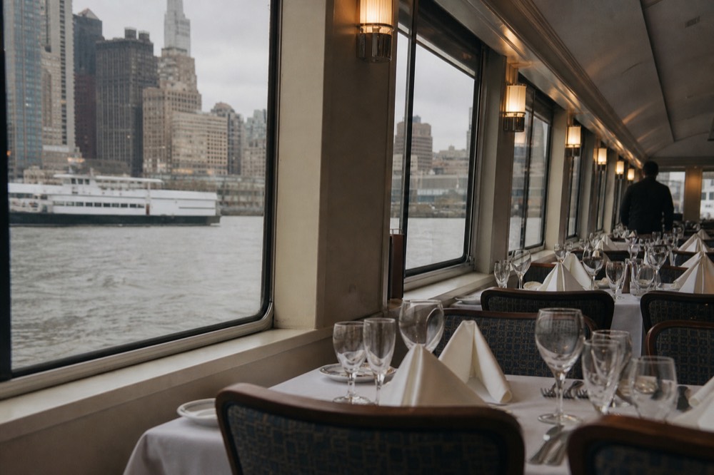 Formal boat dining room set with wine glasses and folded napkins at empty tables, warm lamplight, no diners present