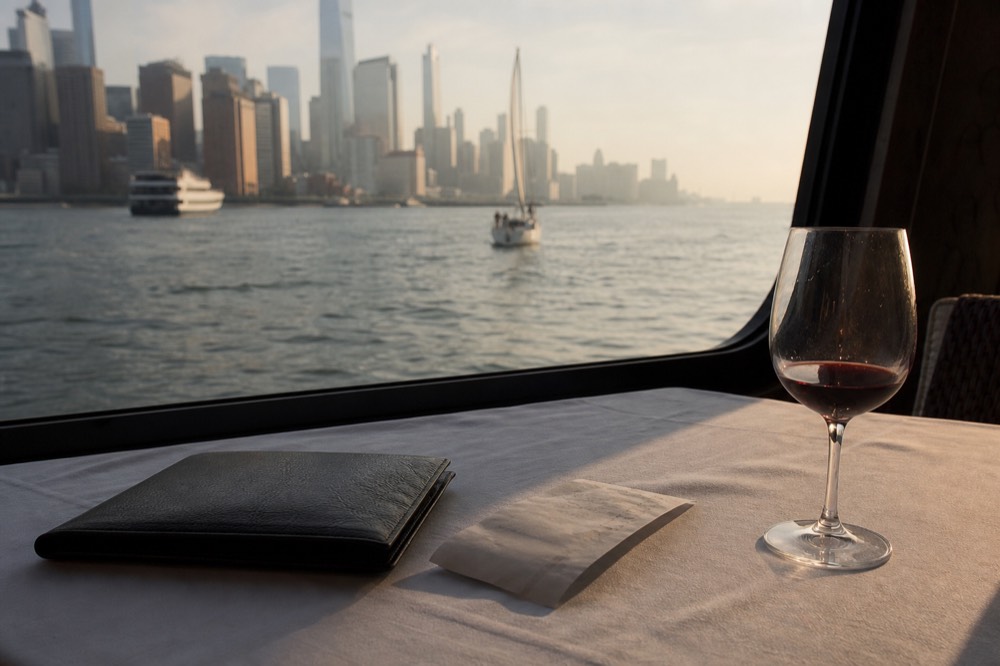 Leather check presenter and a folded receipt on a white tablecloth beside a half-finished glass of wine, boat window dark behind