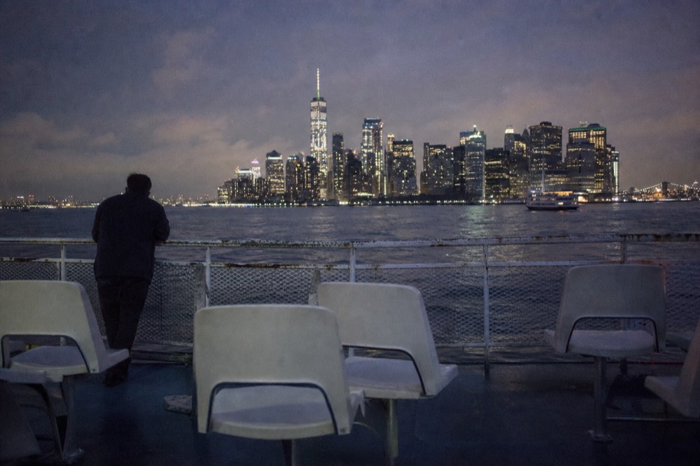 An empty rear deck of a small tour boat at dusk with plastic chairs and a worn railing, harbor water and distant skyline beyond