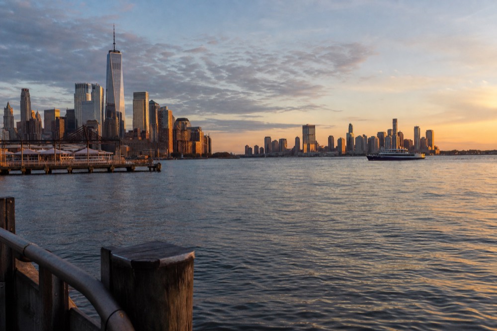 September evening light across the Hudson with sharp detail visible on Midtown towers and a calm water surface reflecting orange