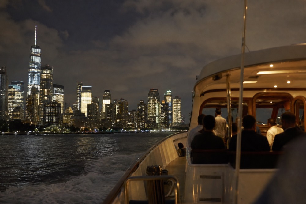 Classic motor yacht under way in golden light with passengers on the open afterdeck and the Manhattan skyline behind