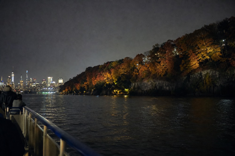 Autumn colour along a wooded riverbank seen from the deck of a boat on the Hudson, orange and red trees above grey cliffs