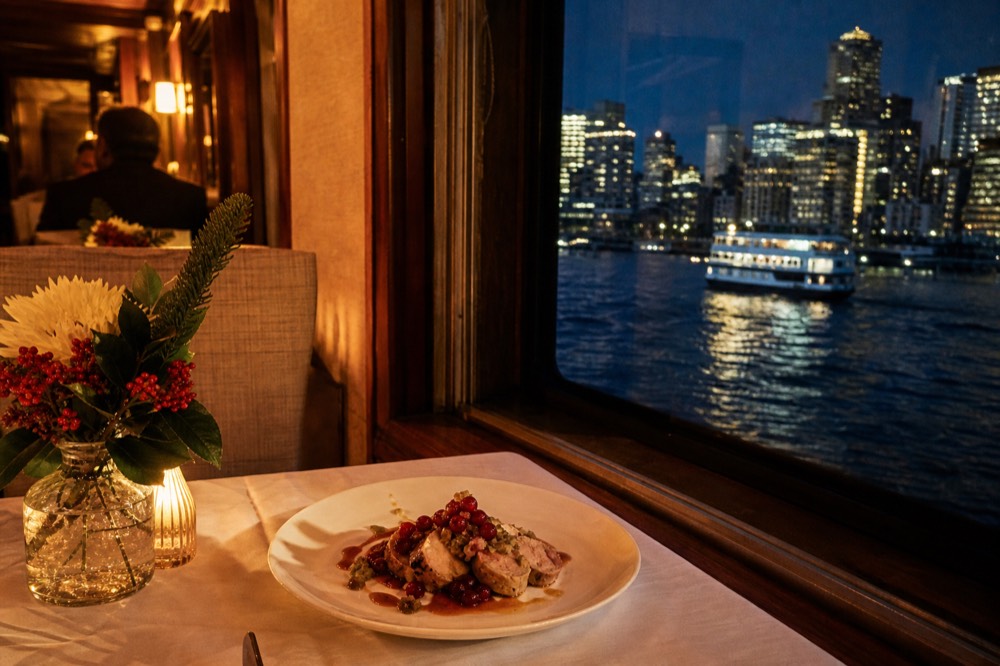A festive plated dinner course with cranberry garnish on a white tablecloth beside a dark window reflecting warm cabin lights