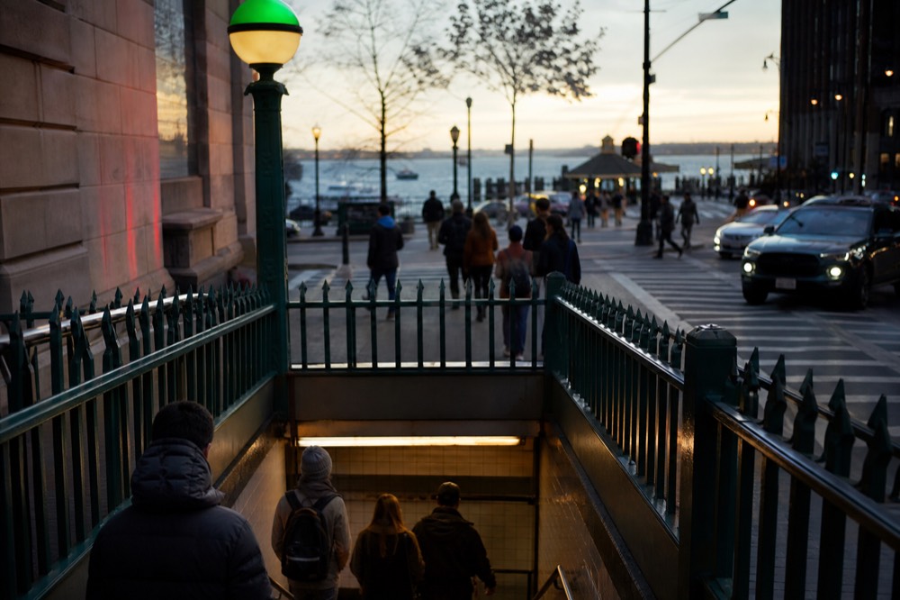 Green subway entrance globe and station stairs on a Manhattan corner with pedestrians heading down in early evening