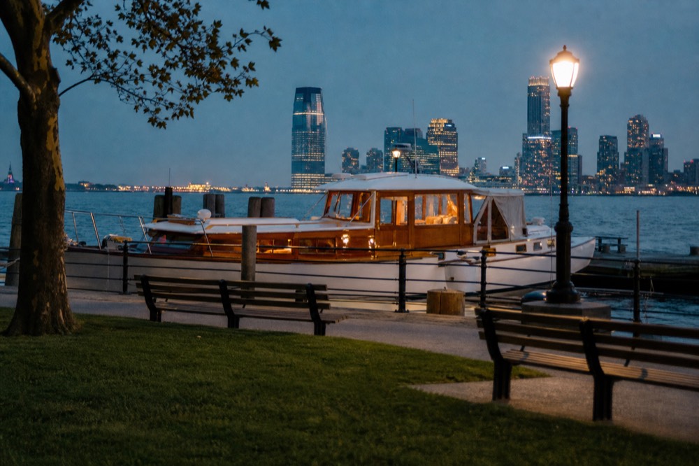 Small classic motor yacht with a varnished deckhouse moored at a park pier with lawn and benches in the foreground
