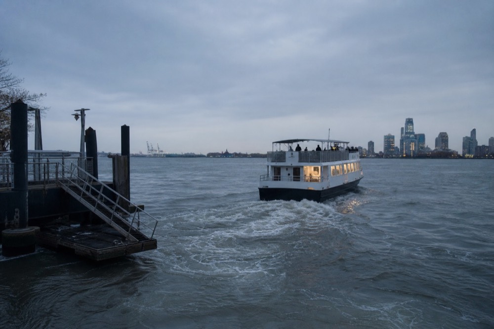 Excursion boat pulling away from a pier at blue hour with its wake spreading and the empty gangway still on the dock