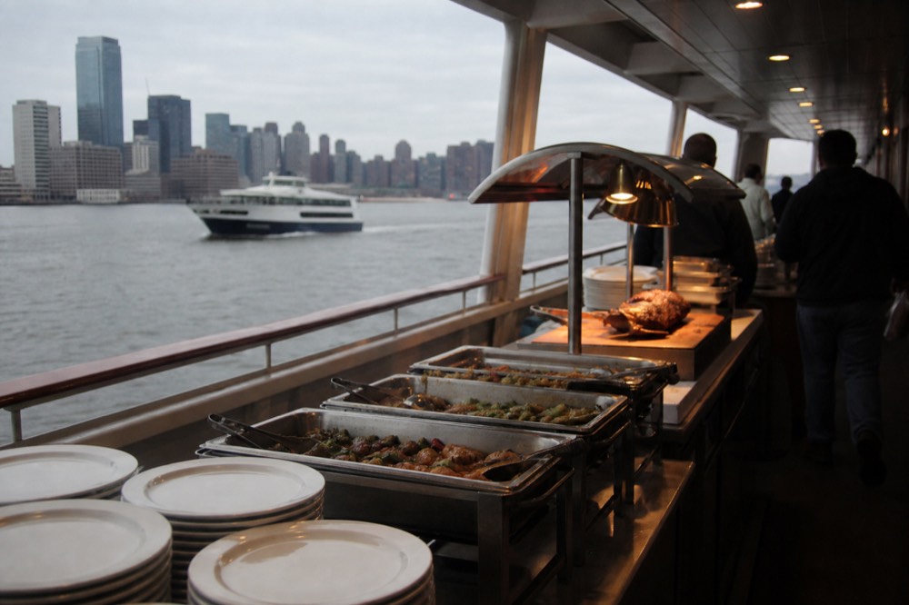 Buffet service line on a cruise vessel with chafing dishes of hot food, a carving station and stacked white plates under warm lighting
