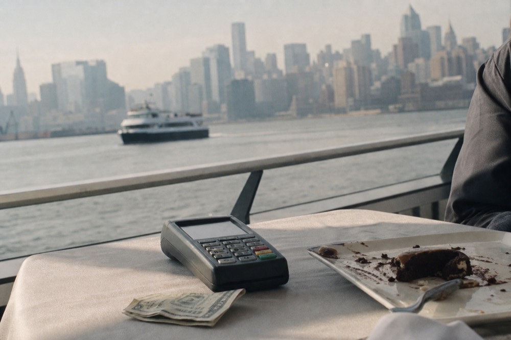 Close view of a folded paper bill and card terminal on a linen-covered boat table with a half-finished dessert plate beside it